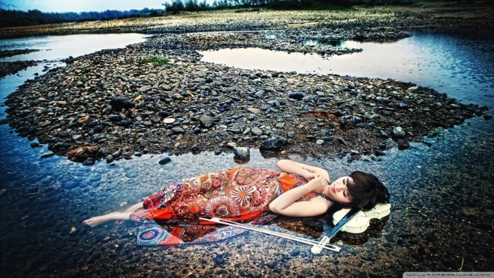 一名穿彩色连衣裙的成年女子躺在布满卵石的浅水河滩上。