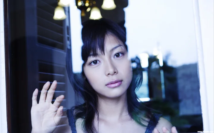 一名成年女性站在窗边，面向镜头抬手靠近玻璃。