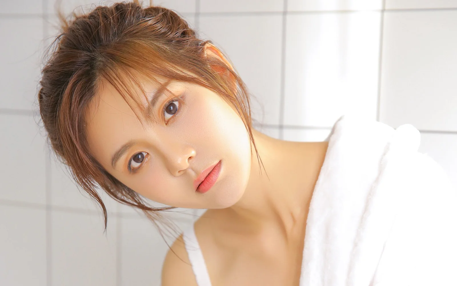 明るい室内で成人女性が頭を傾けてカメラを見つめている。