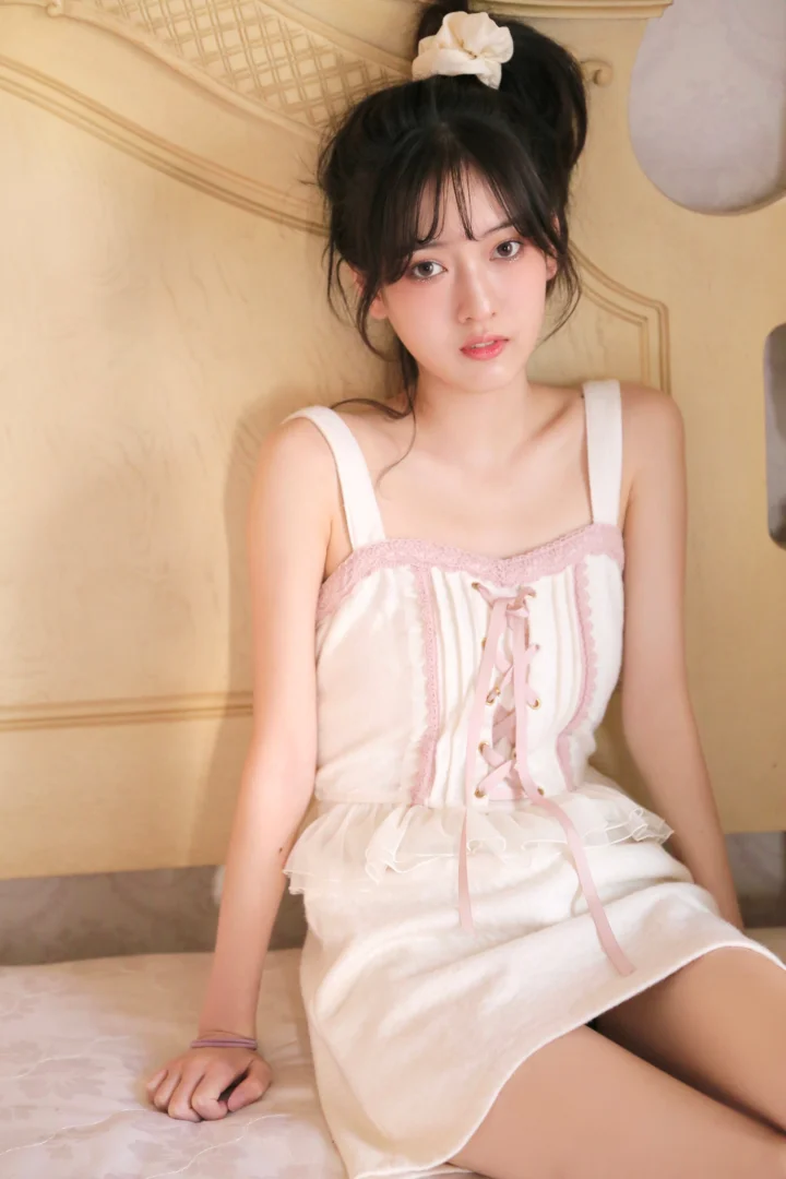 一名身穿白色连衣裙的女性坐在室内床边面对镜头。