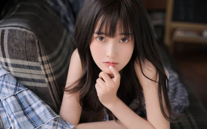 一名长发女性坐在室内，面对镜头并用手托着下巴。