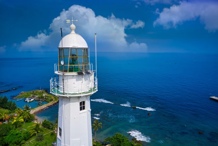 白色灯塔矗立在海岸边，远处是蔚蓝海面和蓬松云朵。
