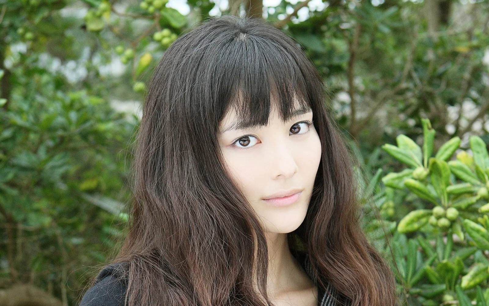 一名长发女性在绿叶植物前的户外肖像。