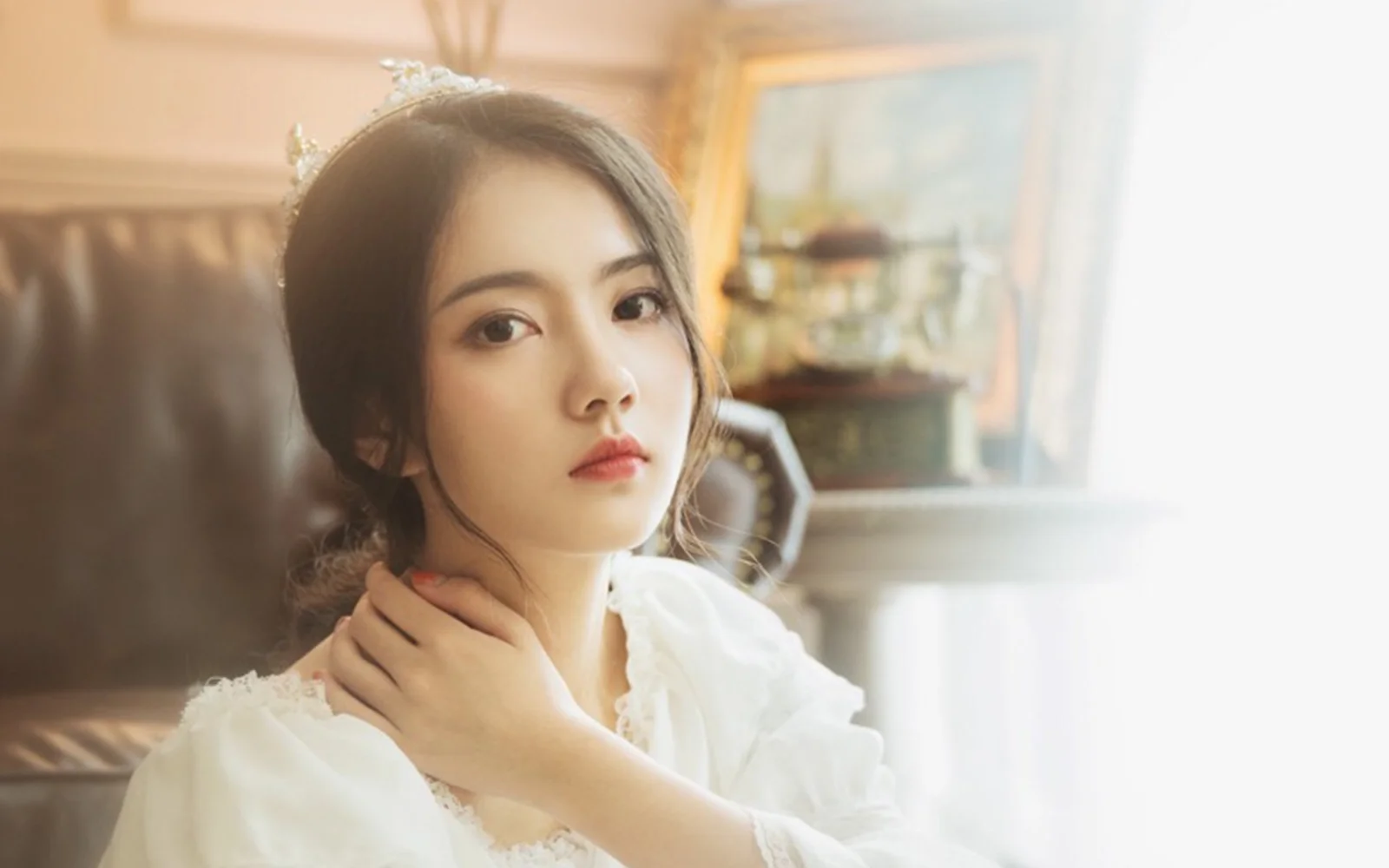 티아라를 쓴 흰색 드레스의 여성이 실내에서 카메라를 바라보고 있습니다.