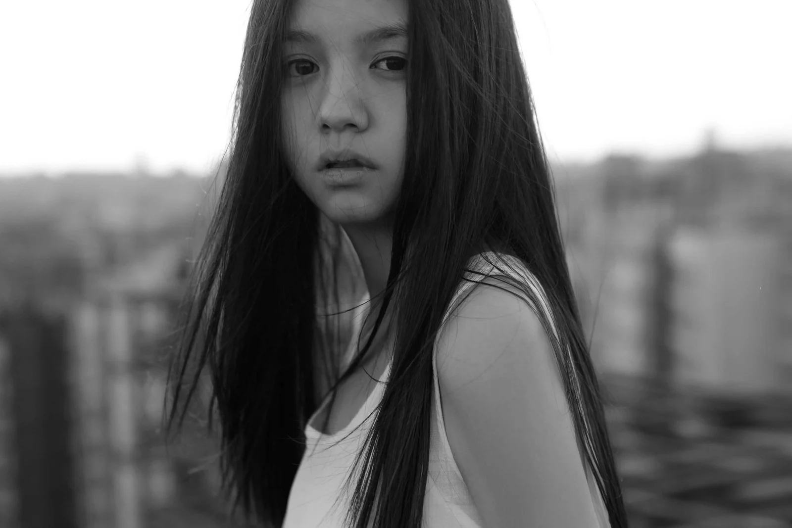 一名长发女性在户外回望镜头，背景是虚化的城市景色。
