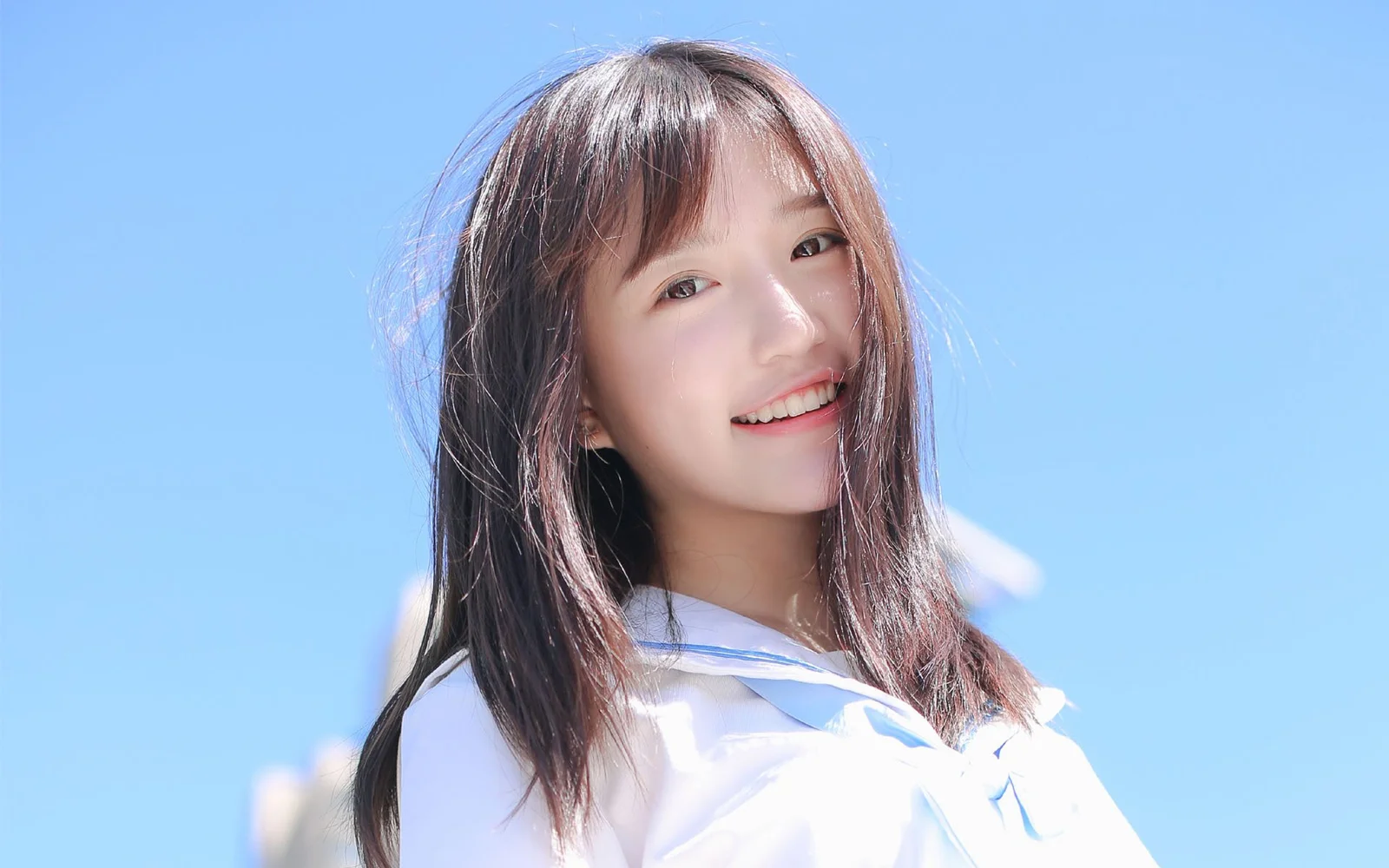 長い髪の女性が明るい青色の背景の前で微笑んでいる。