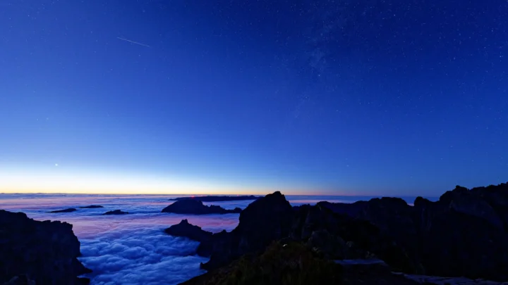 暮色中的深色山峰俯瞰翻涌的云海，远处天空呈现蓝紫色渐变并点缀着星光。