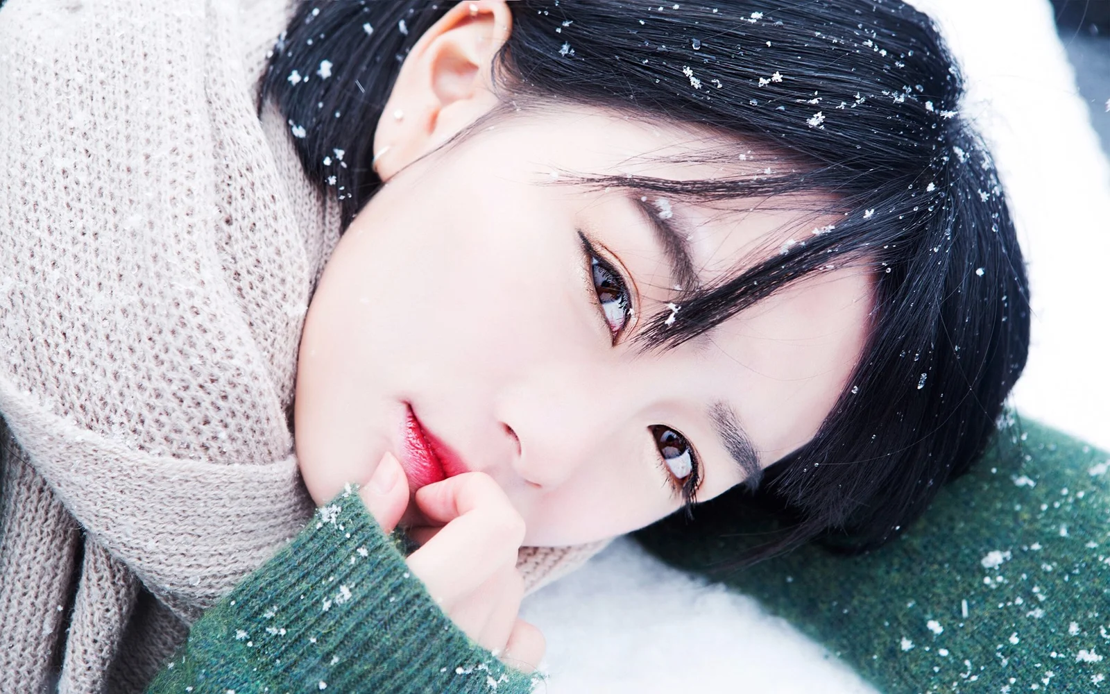 니트 스웨터를 입은 성인 여성이 눈 속에 누워 있으며 머리카락과 얼굴에 눈송이가 내려앉아 있습니다.