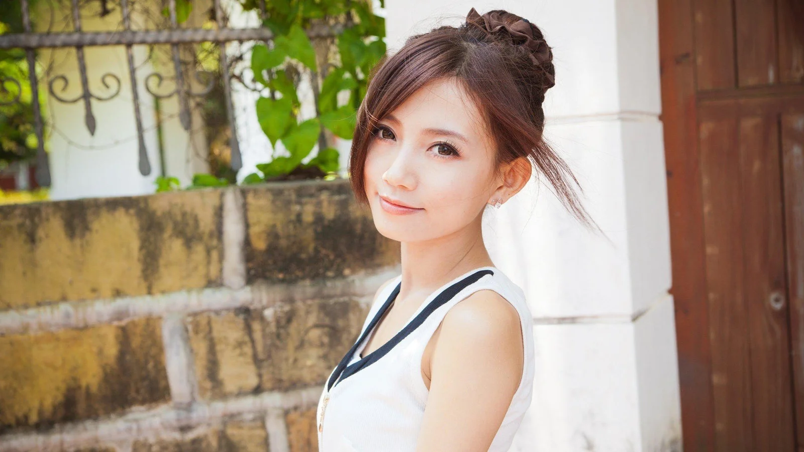 一名成年女性站在带有绿植、石墙和木门的户外建筑旁微笑看向镜头。