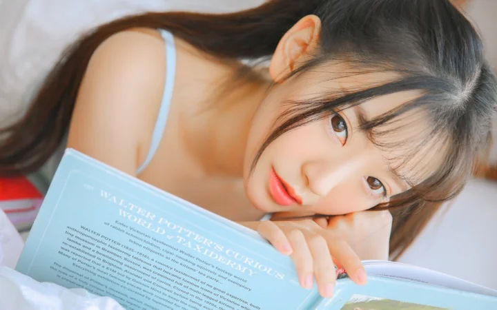 긴 머리의 여성이 누워서 책을 읽고 있다.