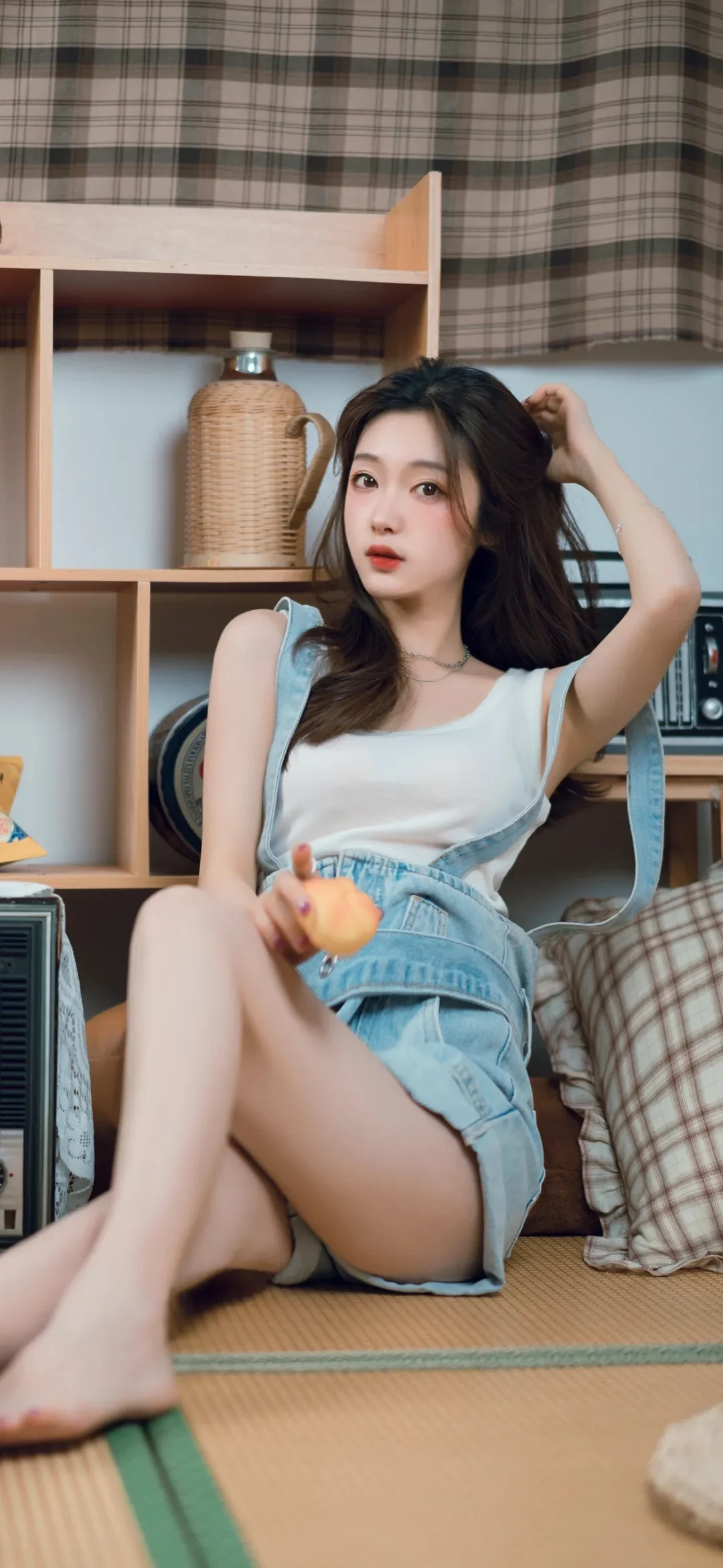 一名成年女性坐在室内藤编和格纹装饰的空间中，手持橙色水果。