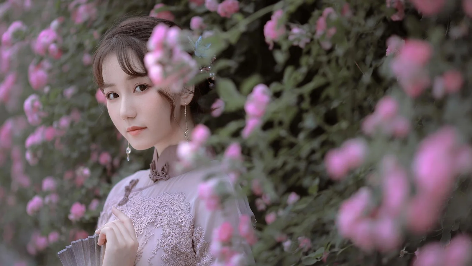 一名身穿传统服饰的女子站在粉色花朵之间。