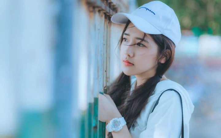 白い帽子をかぶった女性が屋外の古い扉のそばに立っています。