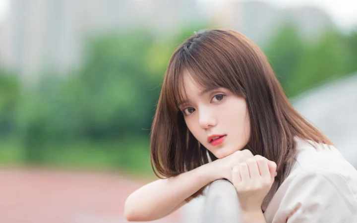 一名棕色长发女性在户外背景前靠着手臂看向镜头。