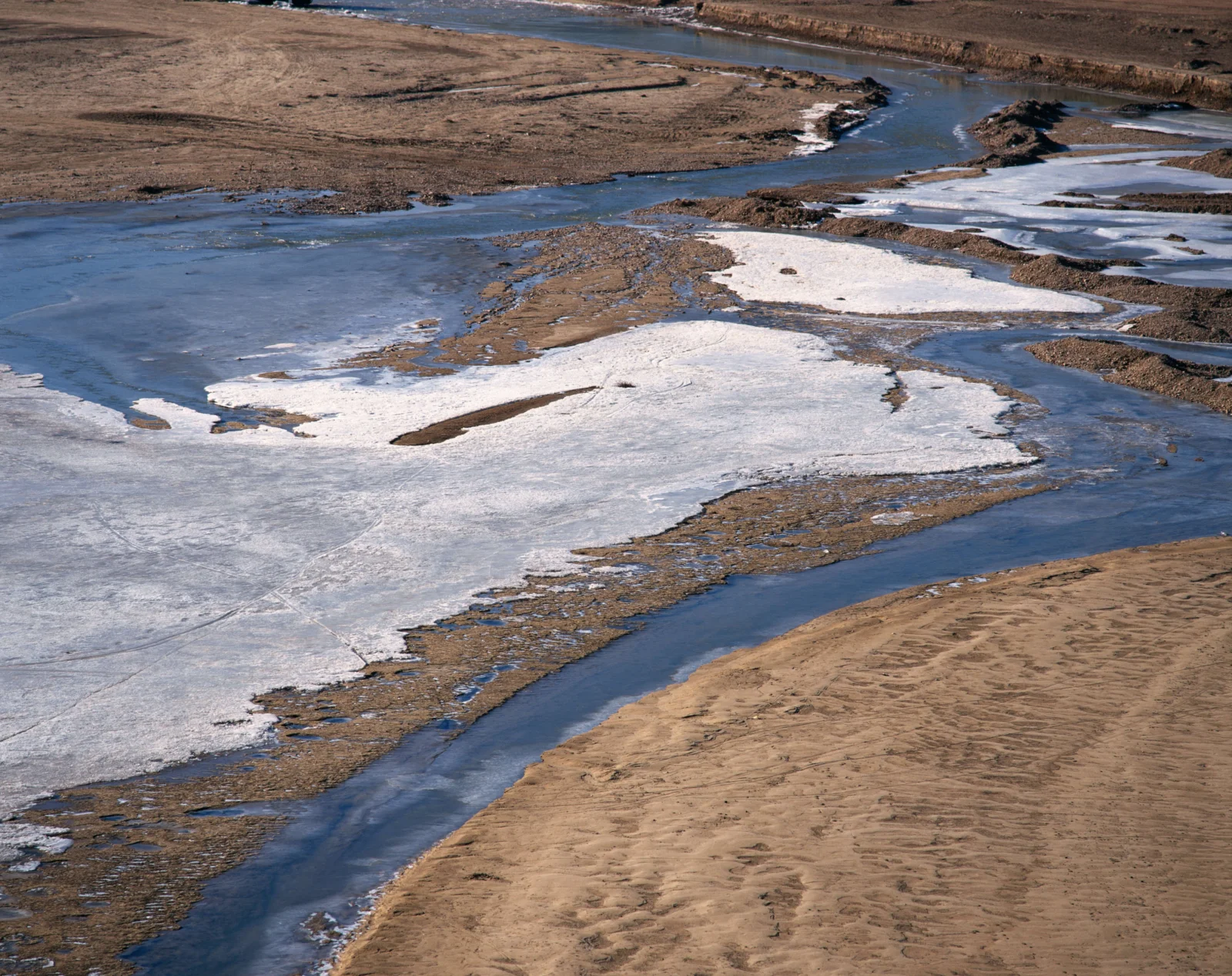 蜿蜒的河道穿过覆盖着冰雪与裸露沙地的冬季地表。