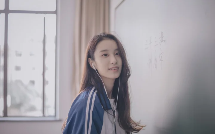 一名戴着有线耳机的女子站在窗边，室内光线柔和。