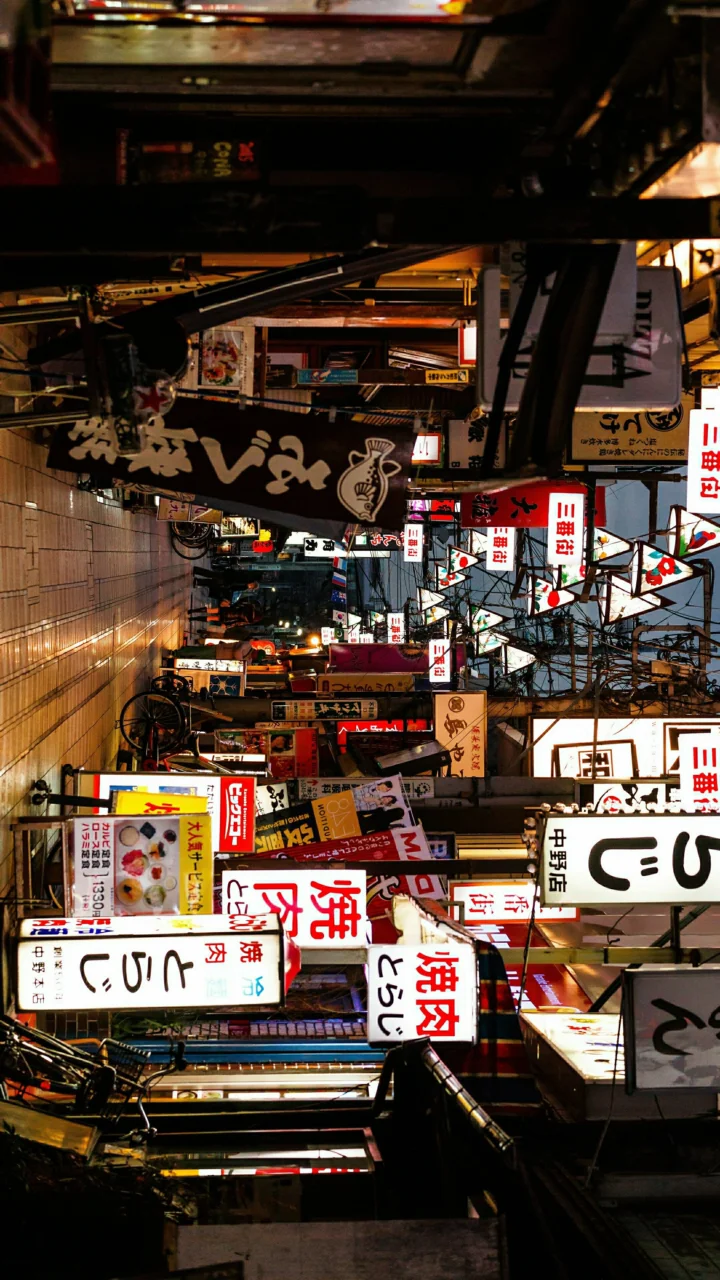 一条狭窄的城市街巷两侧布满店铺、悬挂招牌和明亮的广告牌。