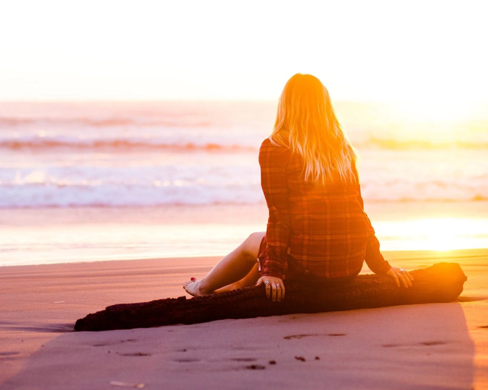 女性がビーチの黒いブランケットに座り、夕日に照らされた海を眺めている。