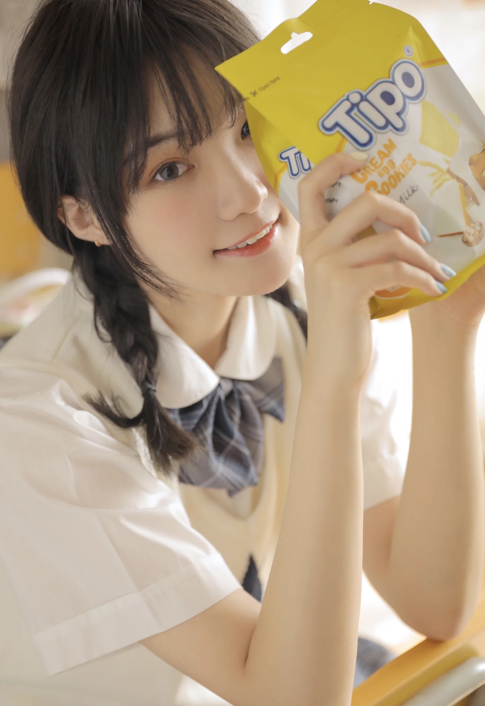一名穿着校服的女子在明亮室内手持黄色零食袋。