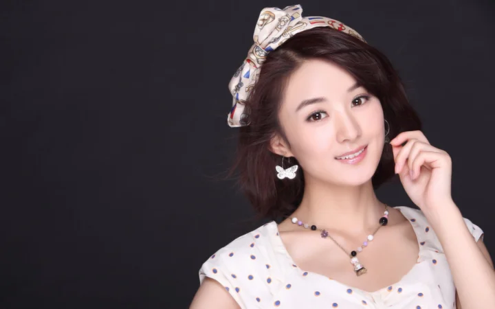 一位成年女性在深色背景前微笑，佩戴发饰、耳环和项链。