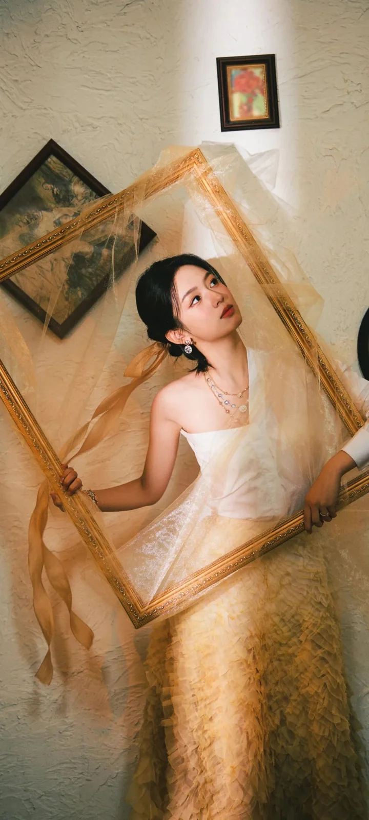 一名身穿白色礼服的女子在室内手持华丽画框。