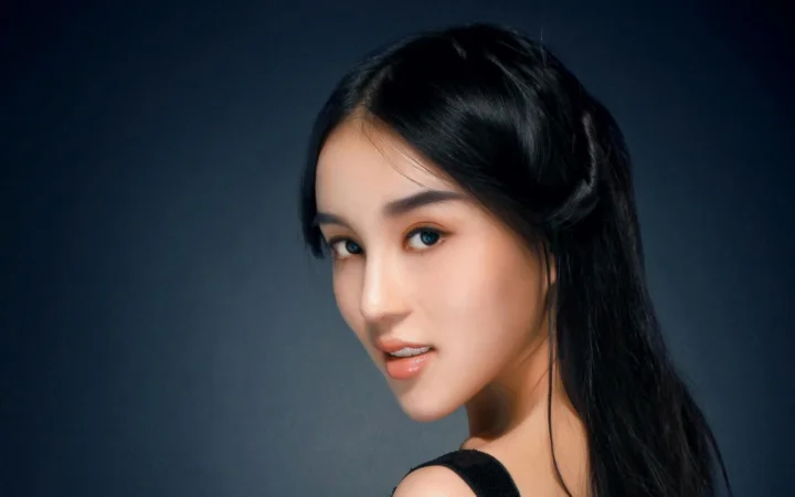 一位黑发女性在深色背景前侧身凝视镜头。