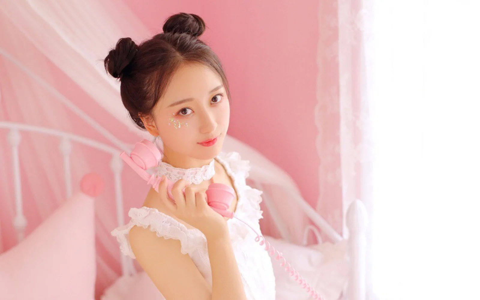 ピンクの寝室でピンクのヘッドホンを身につけた若い女性が、カメラに向かって微笑んでいる。