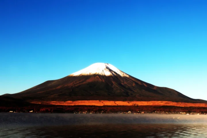 雪顶山峰倒映在湖面上，远处是晴朗的蓝天。