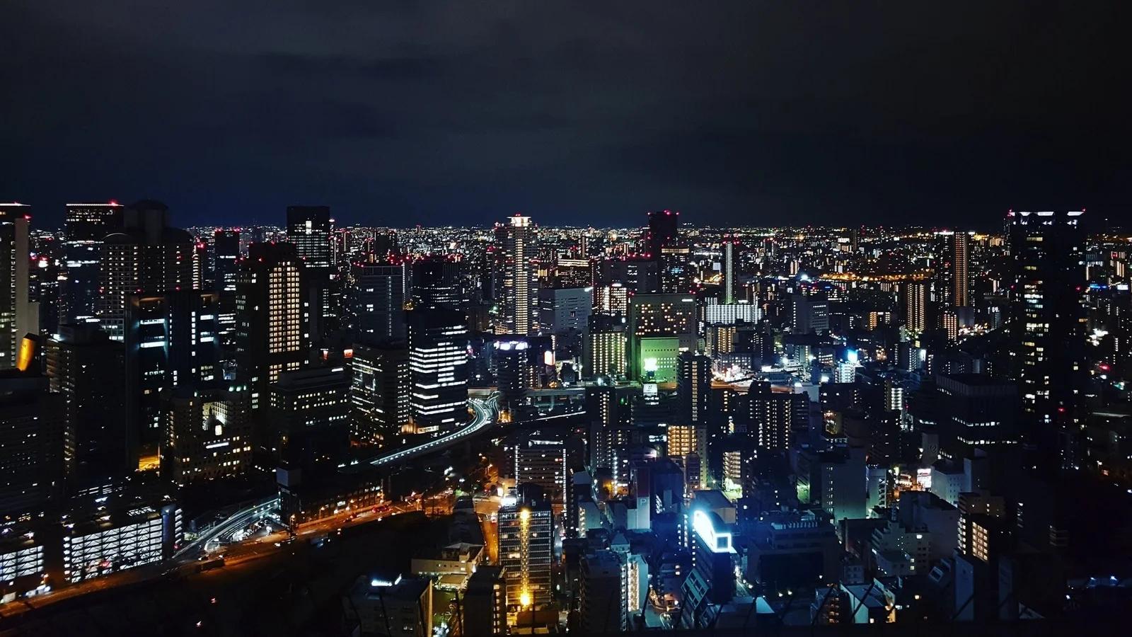 夜色中的城市高楼密集分布，街道与建筑灯光交织成明亮的都市天际线。