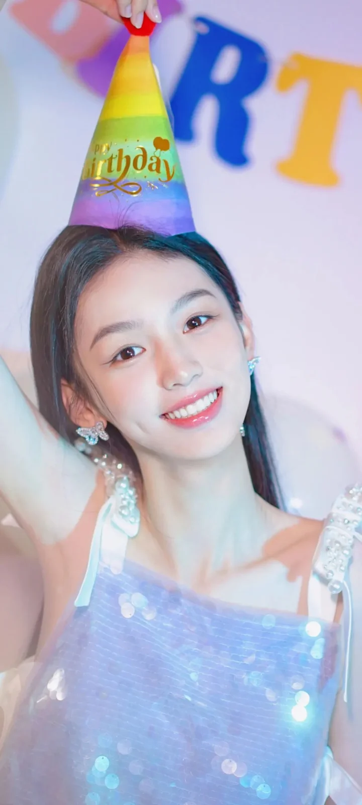 一名女子戴着彩色派对帽微笑面对镜头，身穿带亮片装饰的浅色服装。
