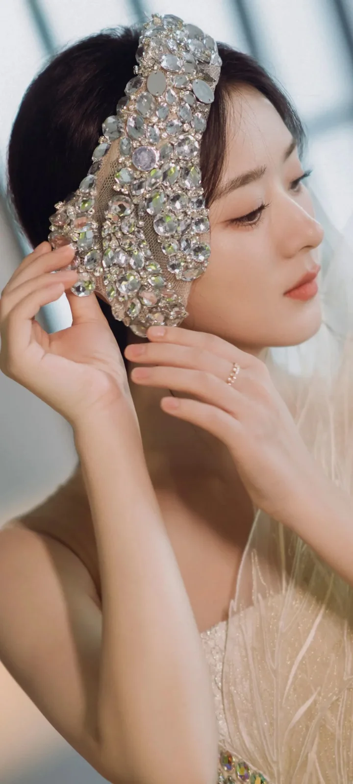 一位成年女性侧身面对镜头，佩戴华丽珠饰头冠并以双手整理头饰。