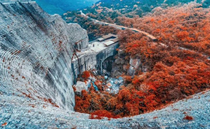 秋日的云台山峡谷中，灰白色岩壁、石桥与红橙色树木交织在一起。