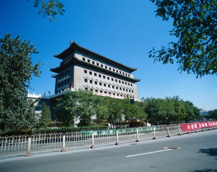 蓝天下，一座传统风格建筑坐落在绿树和街道旁。