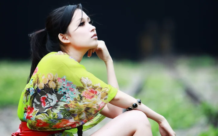一名成年女性穿着花卉图案上衣坐在户外绿地前。