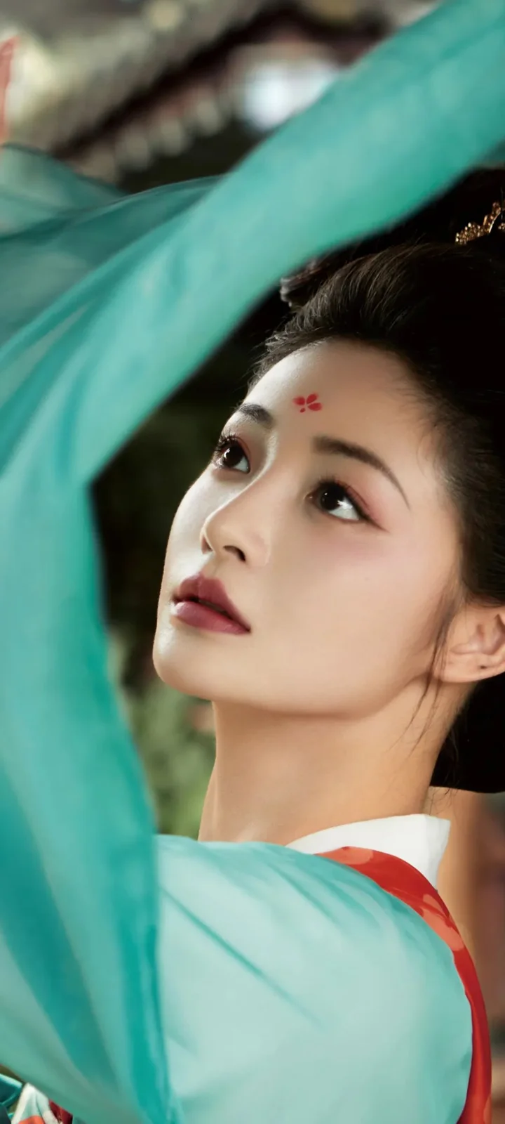 一位身穿浅绿色传统服饰的女性抬头望向上方，面部近景占据画面主体。