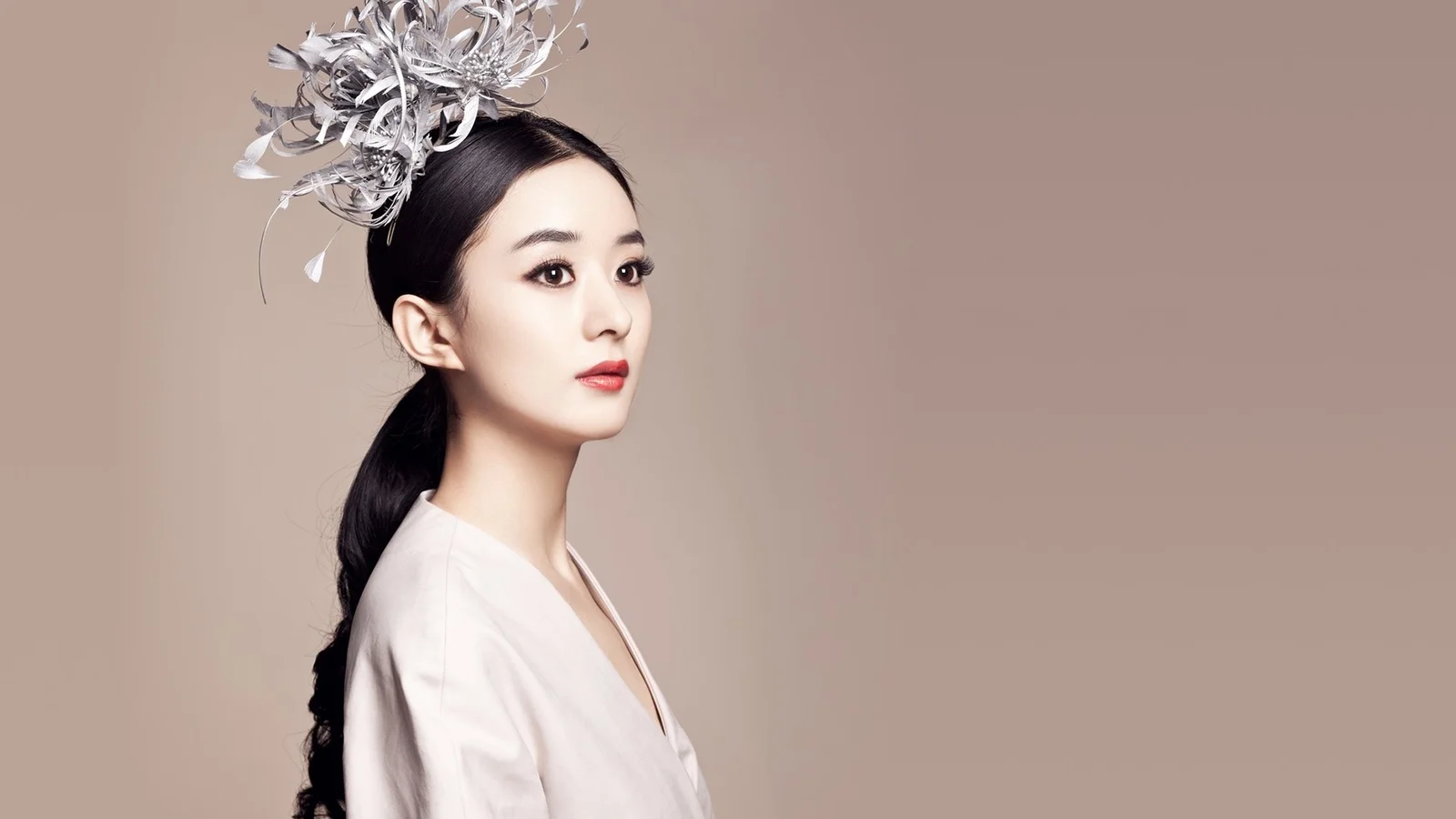 은색 헤드피스를 착용한 성인 여성이 연한 갈색 단색 배경 앞에서 옆모습으로 서 있다.
