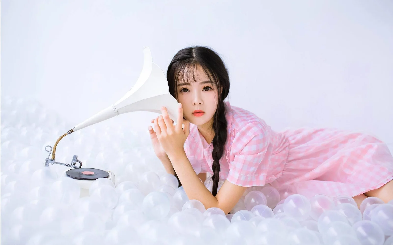 一名身穿粉色格纹连衣裙的女性趴在白色泡沫球上，背景明亮柔和。