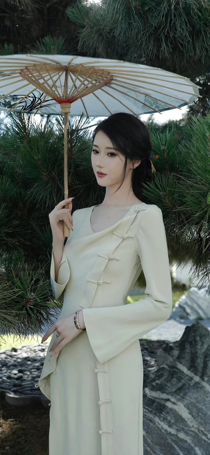 一名女子撑着纸伞站在松树和石景之间。