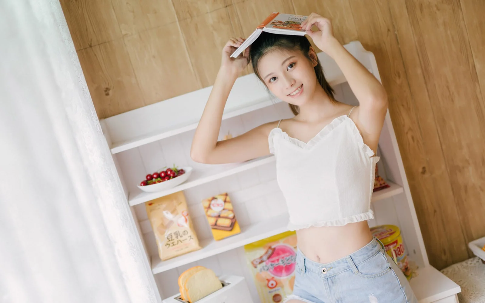 一名女性在室内举着书本，站在木质墙面和置物架前。