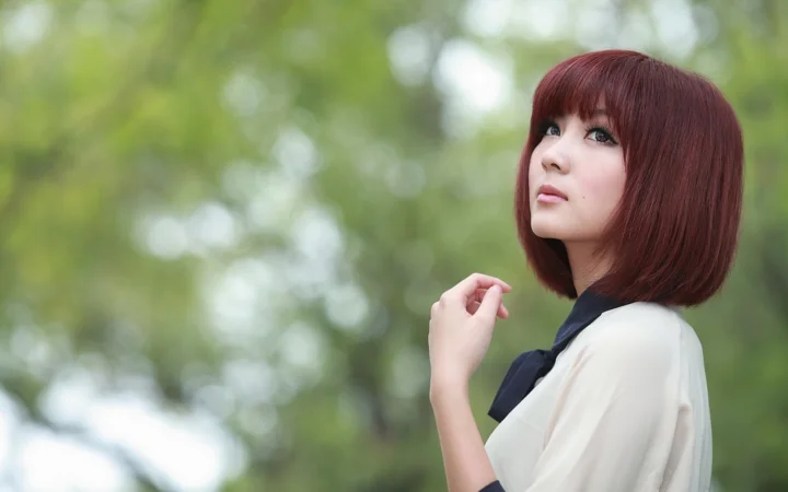 一位红发女子在绿意朦胧的户外背景前回眸凝视。