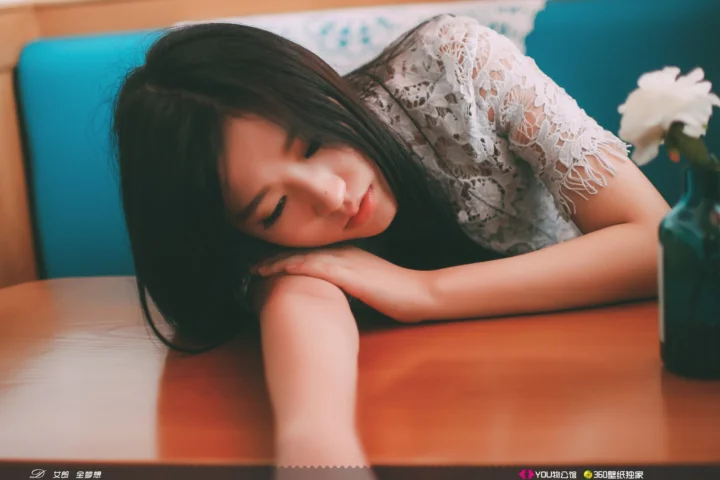 흰색 레이스 상의를 입은 성인 여성이 나무 테이블에 팔을 올리고 쉬고 있습니다.