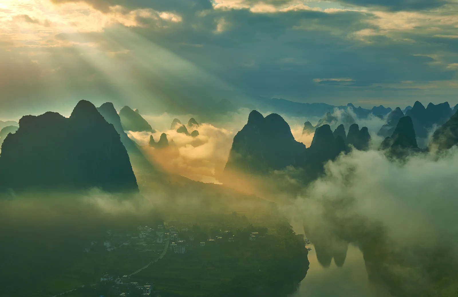 阳光穿过云层，照亮了漓江上空被雾气环绕的喀斯特山峰与河流。