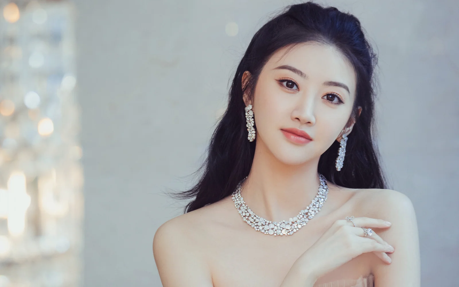 一位佩戴闪亮珠宝的女性面对镜头 posed for a soft studio portrait.