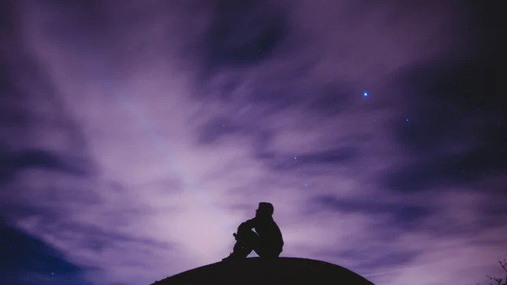 紫色夜空中飘着薄云，繁星点缀天际，前景是一道坐在圆形高处的剪影。