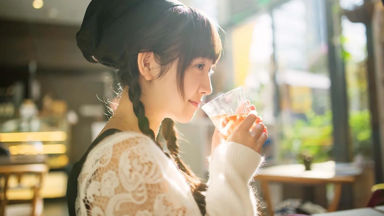 一名成年女子在阳光明亮的咖啡馆里手持玻璃杯。