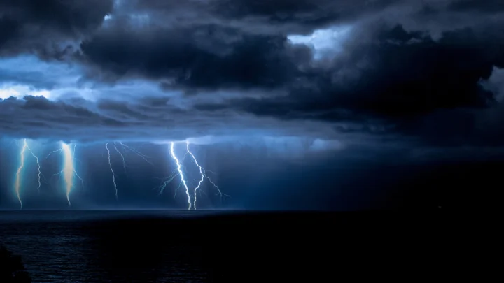 乌云笼罩的海面上闪电划破夜空，呈现出深蓝色的暴风雨景象。