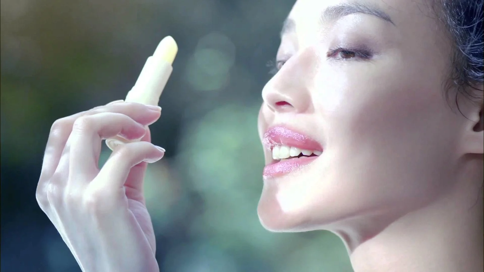女性が唇の近くに口紅を持っている横顔のクローズアップ。