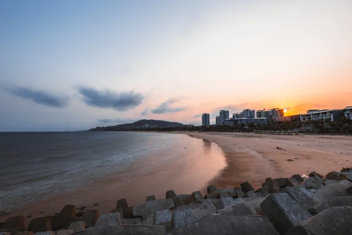 夕阳映照下的海滩、海面与远处建筑构成宁静的海岸景色。