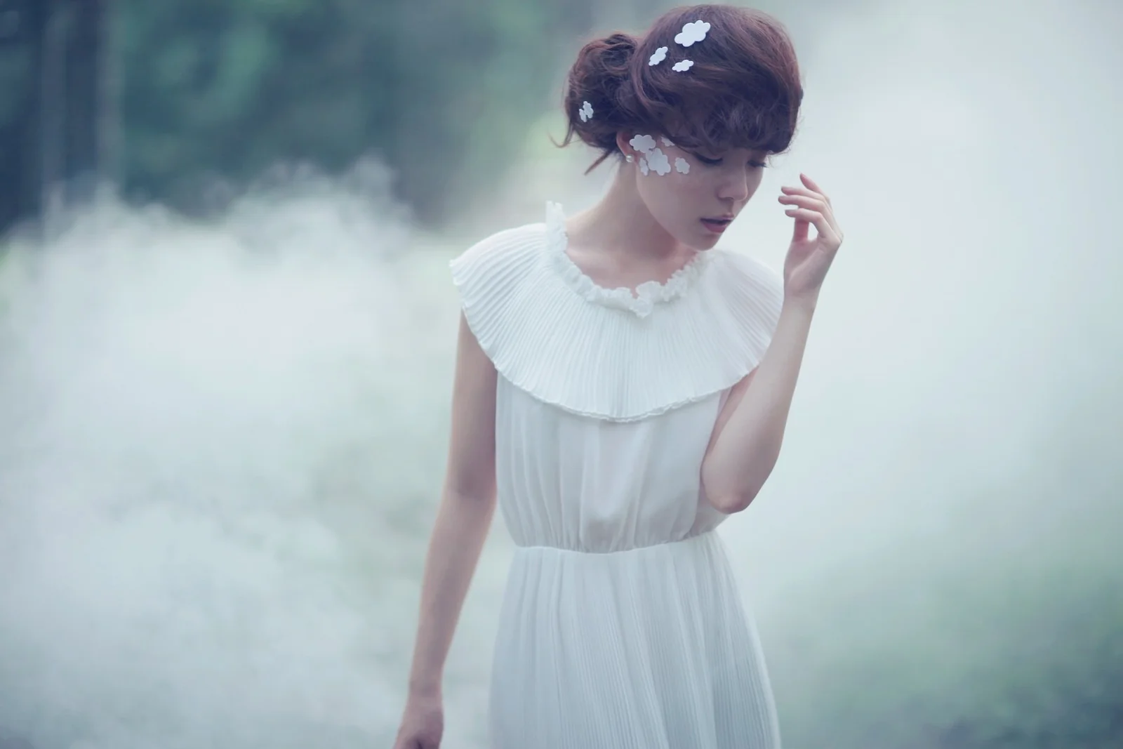 白いワンピースを着た成人女性が、霧の立ち込める林の中に立っています。