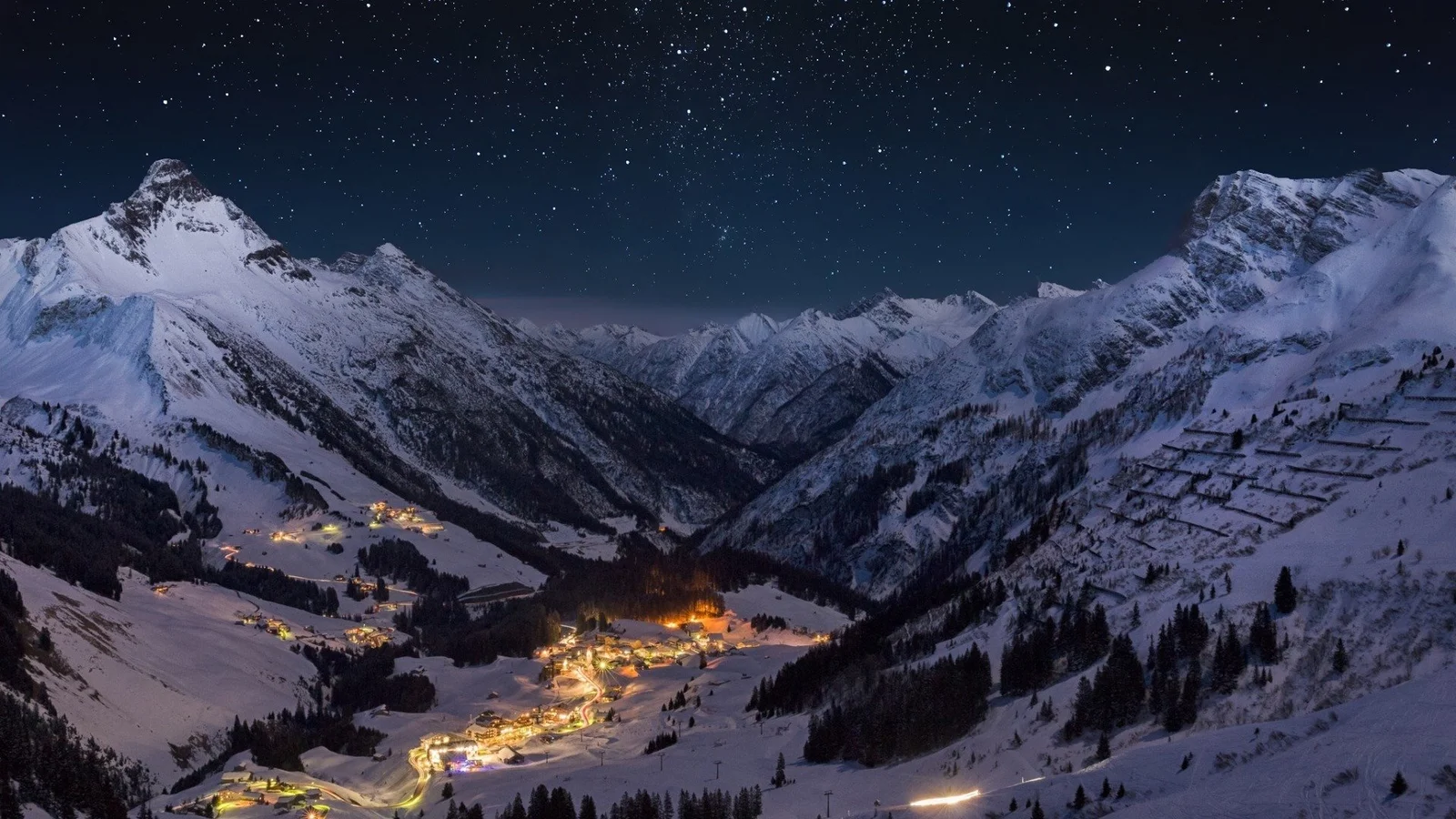 夜空下的积雪山谷中，山脚村落的灯光温暖闪烁。